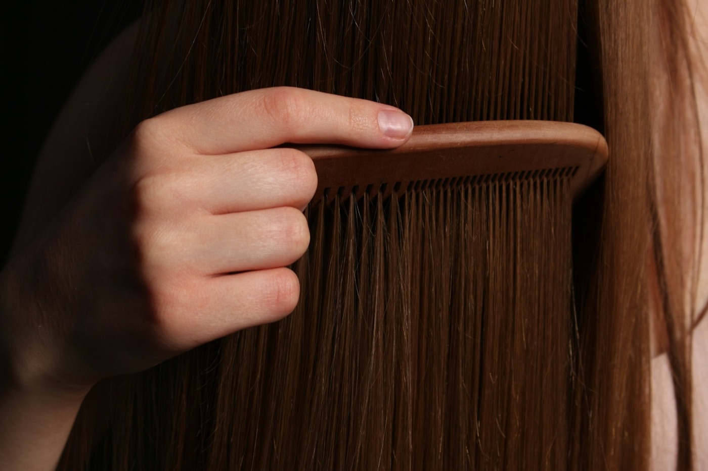 A hand drawing a comb through glossy, healthy lengths of hair