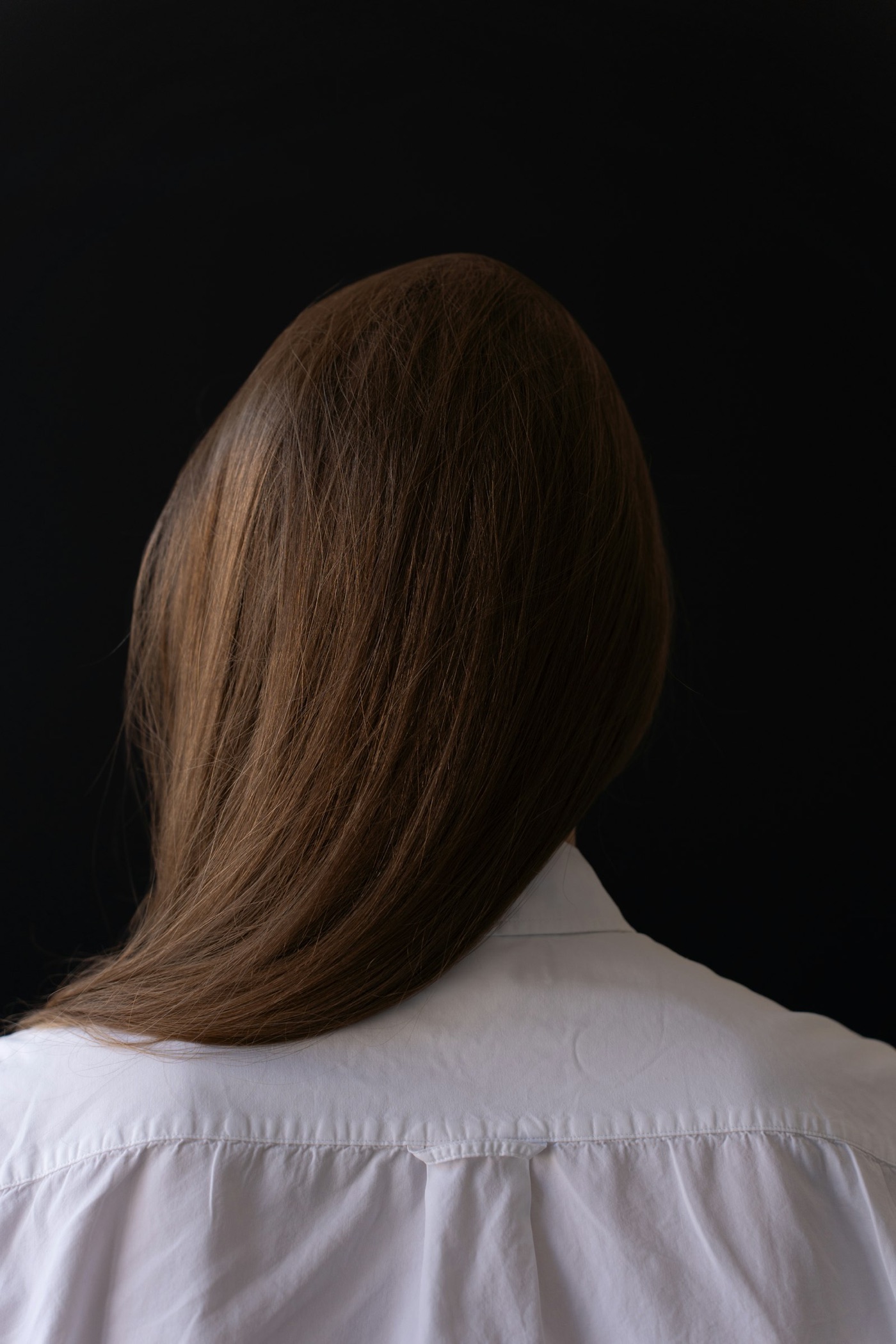Sleek, glass-finish straight hair falling over a white shirt against black